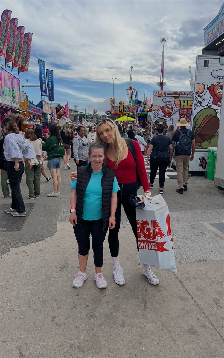 Two people at a showground with rides and stalls behind them